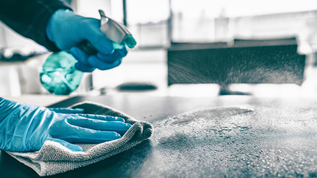 Behandschuhte Hände reinigen eine Küchenarbeitsfläche mit Sprühreiniger