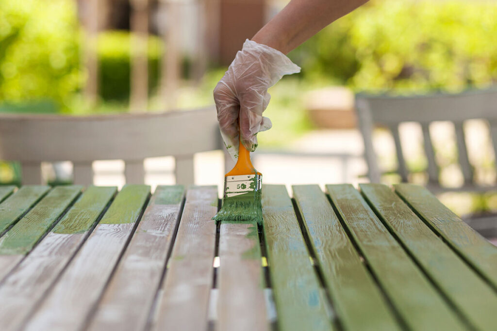 Hand streicht einen Gartentisch aus Holz
