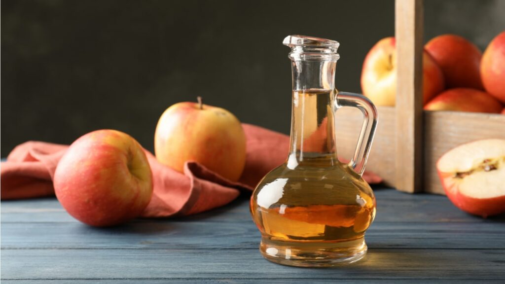 Flasche mit Apfelessig zwischen roten Äpfeln
