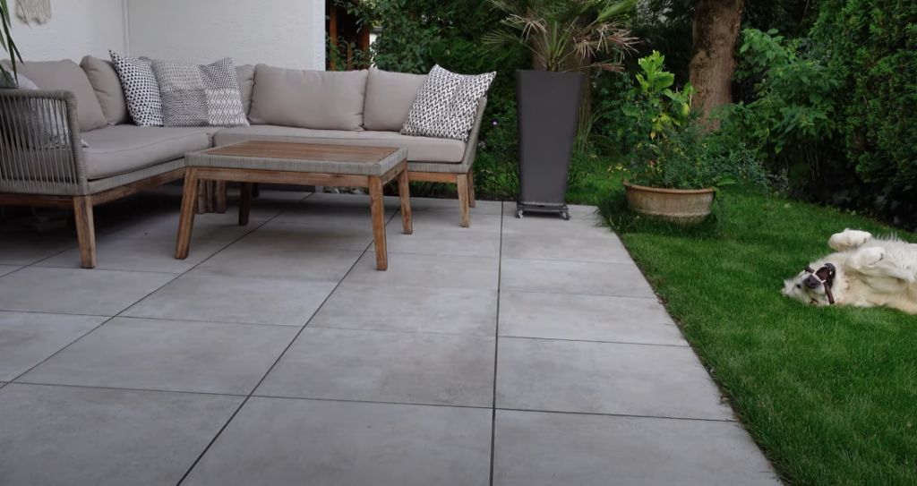 Terrasse aus grauen Platten mit Sitzmöbeln neben einer Rasenfläche
