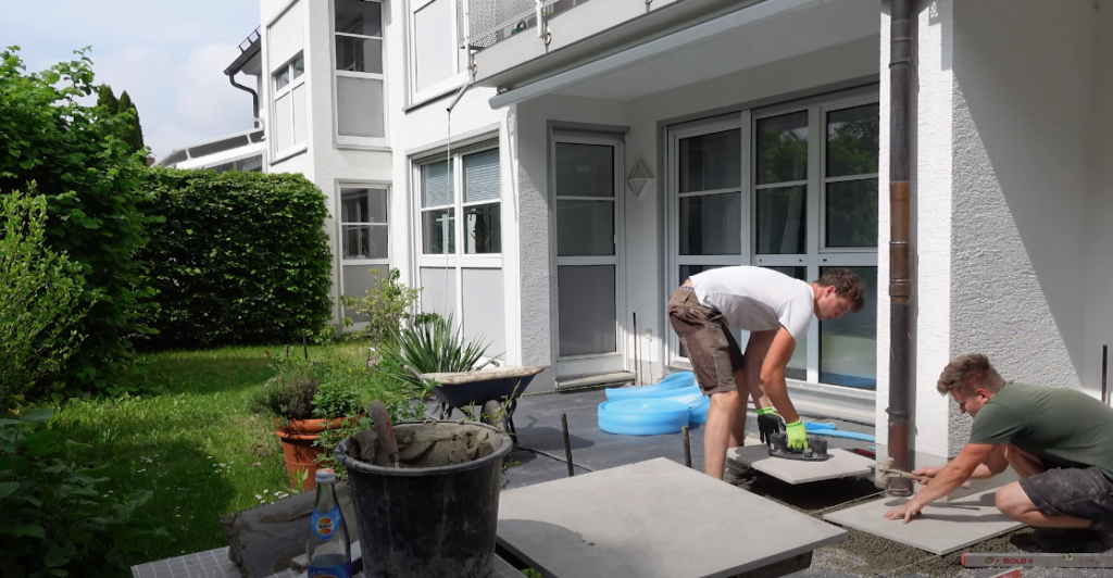 Zwei Männer verlegen großformatige Keramikplatten auf einer Terrasse