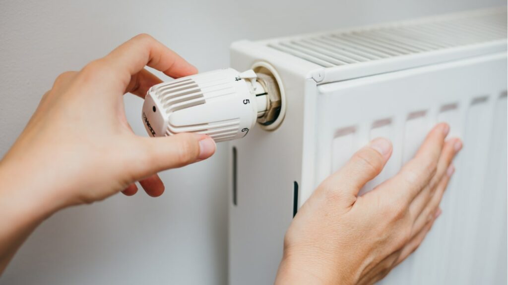 Hand stellt das Thermostat an einem Heizkörper ein