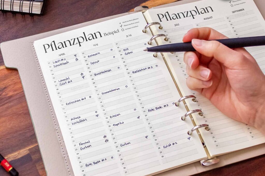 Hand mit Stift über einem geöffneten Pflanzplan