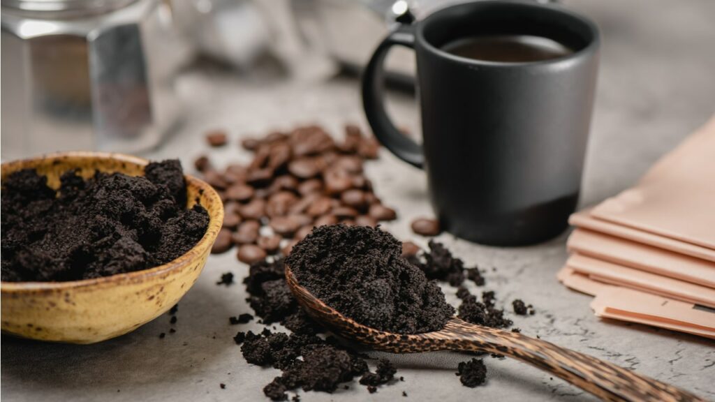 Kaffeesatz auf einem Löffel neben Kaffeebohnen und einer schwarzen Tasse