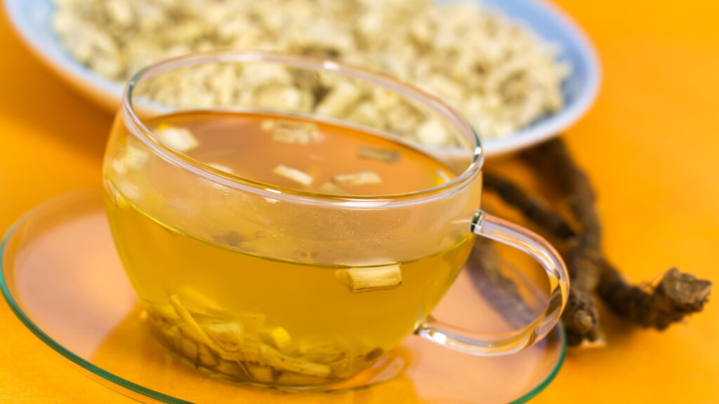 Tasse mit gelbem Eibischtee und getrockneten Wurzelstücken