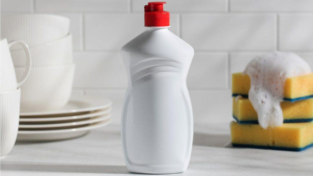 Flasche Spülmittel neben Tellern und Schwämmen
