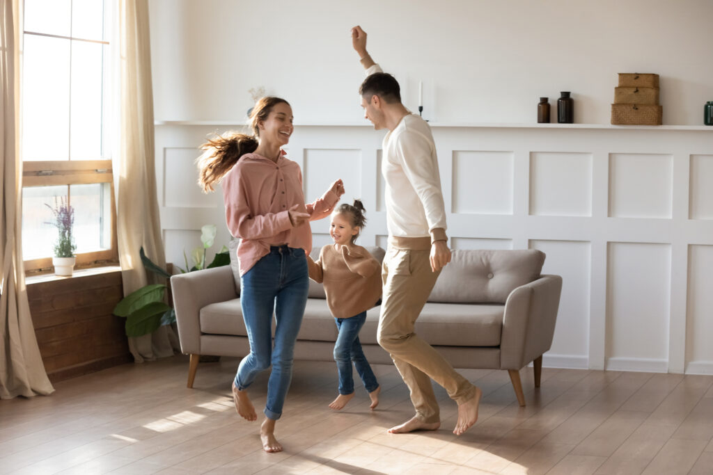 Familie tanzt barfuß in einem hellen Wohnzimmer