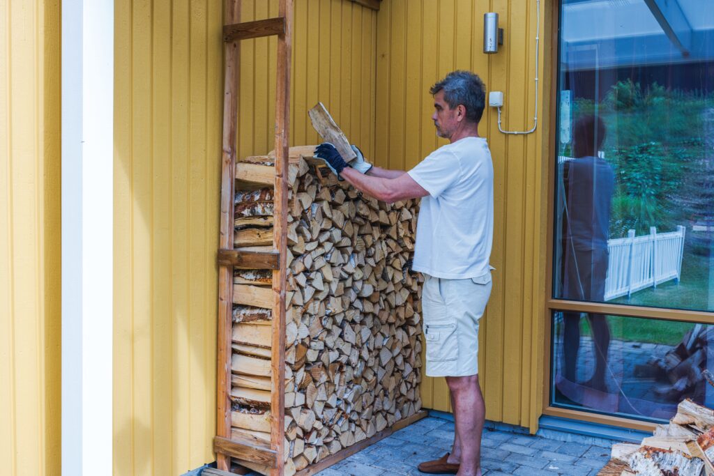 Mann stapelt Brennholz im Unterstand an einer Hauswand