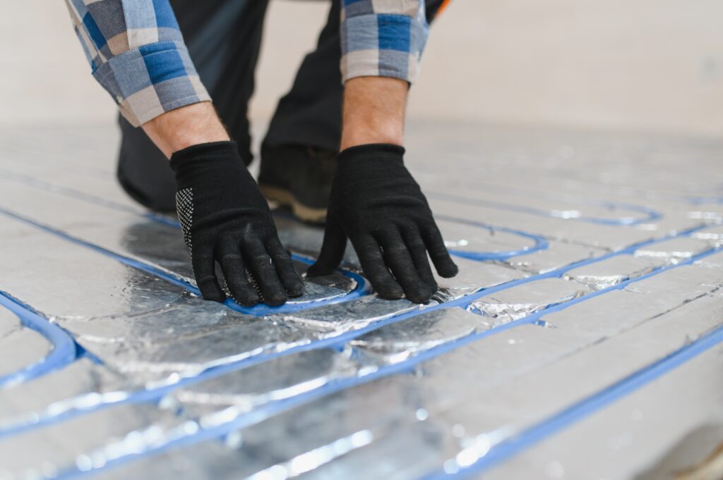Behandschuhte Hände verlegen blaue Heizkabel auf Dämmplatten