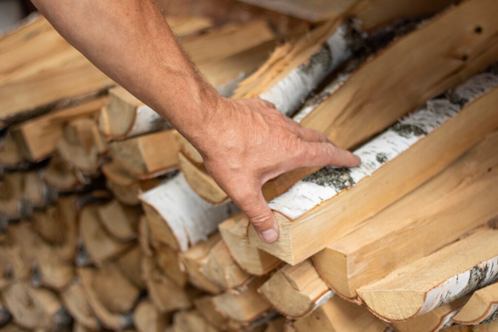 Hand nimmt Birkenholz aus einem Brennholzstapel
