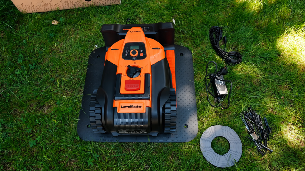 Oranger LawnMaster OcuMow 18 mit Ladestation und Zubehör auf dem Rasen